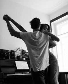 a man and woman standing in front of a piano playing the piano with their arms around each other