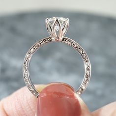 a close up of a person's hand holding a ring with a diamond on it