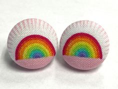 two pink and white buttons with a rainbow painted on it's side, sitting next to each other