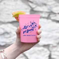 a hand holding a pink flask with a slice of fruit on it