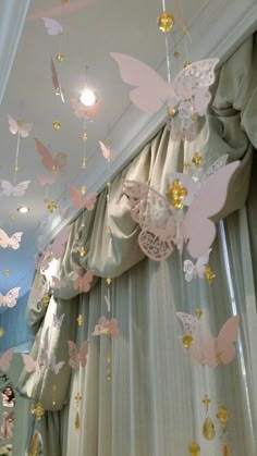 some pink and gold butterflies hanging from the ceiling in a room with sheer drapes