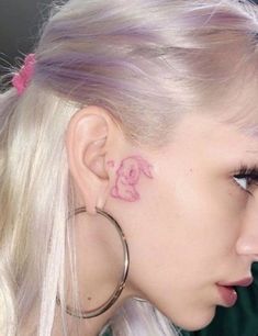 a woman with pink ink on her left ear and behind her ear is an elephant