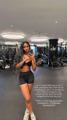 a woman standing in a gym room with her cell phone up to her ear and wearing shorts