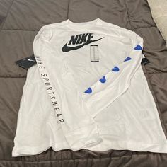 Nwt White Long Sleeve Nike Tee. The Left Sleeve Is Adorned With 5 Blue And White Nike Swoosh Emblems And The Right Arm Has Nike Sportswear Written Down It. The Back Of The Shirt Has The Nike Emblem Written Backwards. Nike Tee, White Nike, Nike Swoosh, Nike Tees, Boys Top, Kids Nike, Nike Shirts, White Nikes, Nike Sportswear