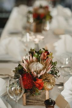 the table is set with white linens and red flowers in a wooden box on it