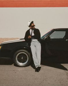 a man sitting on the hood of a car in front of a building with his arms crossed