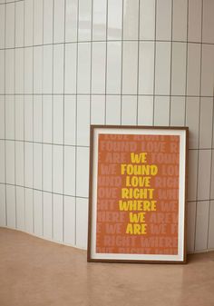 an orange and yellow poster with words on it sitting in front of a white tiled wall