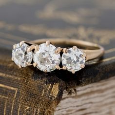 three stone diamond ring sitting on top of an old book with gold trimmings