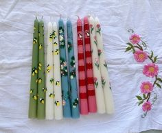 five candles are lined up on a white tablecloth with pink flowers and daisies