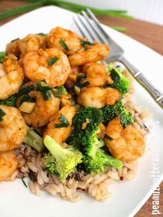 a white plate topped with shrimp and broccoli on top of rice next to a fork