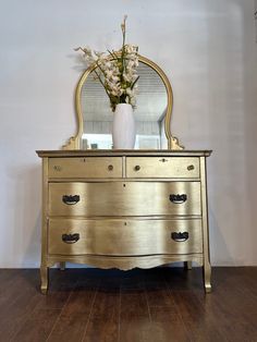 a gold dresser with mirror and flowers on top