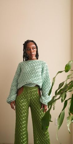 a woman standing in front of a plant wearing green pants and a cropped top