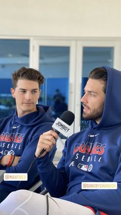 two men in blue hoodies sitting down and one is holding a microphone