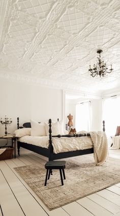 a bedroom with white walls and wood flooring has a chandelier hanging from the ceiling