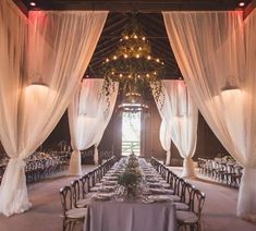 an indoor wedding venue with white draping and chandeliers hanging from the ceiling