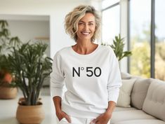 a woman standing in front of a couch wearing a white sweatshirt with the number 50 printed on it