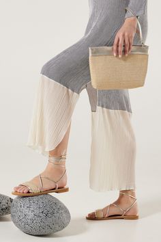 a woman is holding a purse and standing next to a rock with her foot on the ground