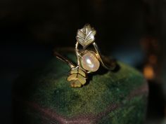 This lyrical Art Nouveau ring by René Lalique is designed around two greenish champleve-enameled leaves gently embracing a natural baroque pearl- depicting an early autumn scene with an acorn and oak leaves just in the process of turning yellow. (In the closeup shots, you can see how he masterfully captured the green leaves gradually turning yellow with subtle golden hue.) Nature and four seasons had been a central theme for Lalique's creations, which is artistically crystalized in this Art Nouveau ring dating from circa 1900.  Signed  "Lalique" and makers mark stamped. Another version of this design by René Lalique featuring a button pearl and enameled leaves is stocked in Hashimoto collection , being pictured in 'Historic Rings' by Diana Scarisbrick  (See pic.10)  Pearls were the favorit Art Nouveau Ring, Acorn And Oak, Mighty Oaks, Jewellery Photography, Celtic Symbols, Life Symbol, Early Autumn, Autumn Scenes, Oak Leaves