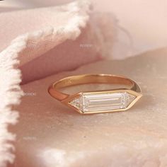 a gold ring with a baguette cut diamond in the middle on a pink blanket