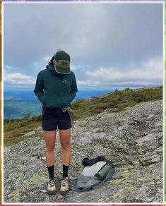 a woman standing on top of a mountain next to a backpack