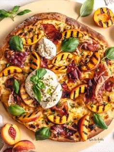 a pizza with peaches, cheese and herbs on it sitting on a plate next to sliced peaches