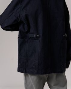 The Recycled Cotton Denim Jacket is a heavy-weight denim chore coat. The jacket features a folded collar, button front, pocket with a pen holder on the left breast, buttoned size adjusters on the back, and dual wraparound pockets at the waist on each side. The material is a 12.6oz recycled denim with reinforced stitching. Cotton Outerwear With Multiple Pockets In Dark Wash, Dark Wash Cotton Outerwear With Multiple Pockets, Dark Wash Cotton Utility Jacket With Flap Pockets, Denim Outerwear With Multiple Pockets For Work, Navy Button-up Utility Jacket With Pockets, Dark Wash Outerwear With Patch Pockets For Everyday, Everyday Dark Wash Outerwear With Patch Pockets, Navy Cotton Utility Jacket With Patch Pockets, Utility Style Cotton Denim Jacket With Multiple Pockets