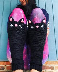 a woman sitting on top of a brick wall wearing black crocheted cat leg warmers