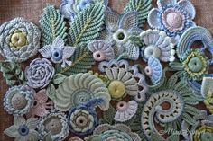 an assortment of crocheted flowers and leaves on a piece of cloth with thread