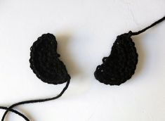 two crocheted pieces of black yarn on a white surface, one has a string attached to it