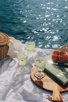 two glasses and a book on a table by the water