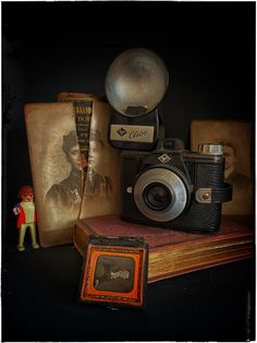 an old fashioned camera sitting on top of a book next to a small figurine