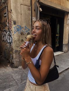 a woman eating an ice cream cone on the side of the road in front of a building