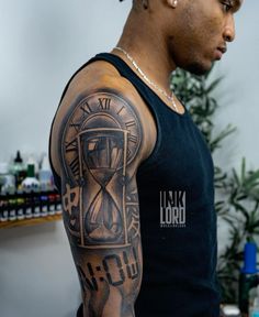 a man with a tattoo on his arm wearing a black tank top that has an hourglass in it