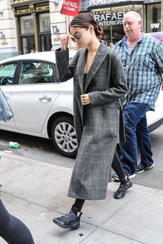 the woman is walking down the street talking on her cell phone while wearing a long coat