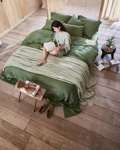 a woman sitting on top of a green bed in a bedroom next to a wooden floor