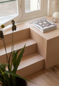 a plant is sitting on some steps in front of a window with a book and vase