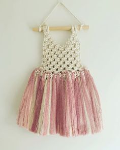 a pink and white dress hanging from a wooden hanger on a wall next to a white wall