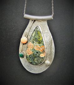 Hammered sterling silver pendant sports a large, fascinating and rich green and peach ocean jasper.  The stone is surrounded by sterling wire and coral and malachite stones and a larger sterling orb.  The piece is topped by a large sterling tube with a substantial sterling link chain.  You definately won't see anyone else with this statement piece as it is an original artisan one of a kind item! Silver Ocean Jasper Necklace, Unique Silver Ocean Jasper Necklaces, Unique Silver Ocean Jasper Jewelry, Artisan Green Ocean Jasper Jewelry, Unique One-of-a-kind Ocean Jasper Jewelry, Distinctive Green Jasper Jewelry, Green Chrysocolla Jewelry With Large Pendant, Unique Jasper Jewelry With Large Pendant, Unique Silver Malachite Jewelry