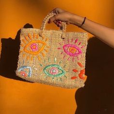 a woman's hand holding a woven bag with an eye design on the handle