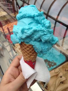 a hand holding an ice cream cone with blue icing