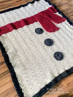 a crocheted snowman blanket sitting on top of a wooden floor