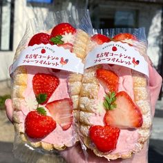 two strawberry shortcakes are wrapped in plastic and have strawberries on the top