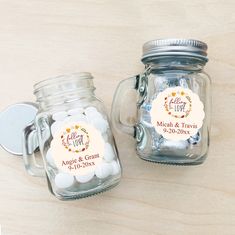 two mason jars with wedding favors in them sitting on a wooden table next to each other