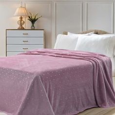 a bed covered in a pink blanket next to a night stand