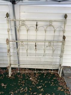 an old white iron bed frame sitting in front of a house with leaves on the ground