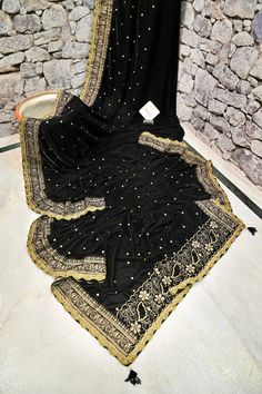 Be the one to shop this designer velvet look first with IndyVogue. Made with soft velvet fabric, it features intricate zari embroidery all over, created using a special machine. The lace border is adorned with delicate mirrorwork, and the pallu has tassels hanging from it. Elevate your ethnic wardrobe with this unique and luxurious saree. Color: A shade of black color Technique: An enriching work of zari embroidery with a lace border with mirror work and tassels on the pallu. Fabric: Velvet