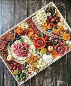 an assortment of cheeses, meats and fruit arranged in a tray on a wooden table