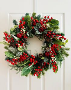 a christmas wreath hanging on a door with pine cones, holly berries and evergreen leaves