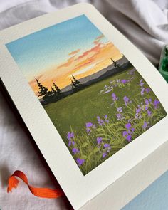 a painting of purple flowers and trees in the background with a ribbon tied to it