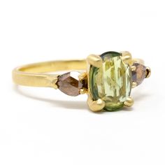 an oval cut green tourmaline surrounded by three brown diamonds in a yellow gold ring